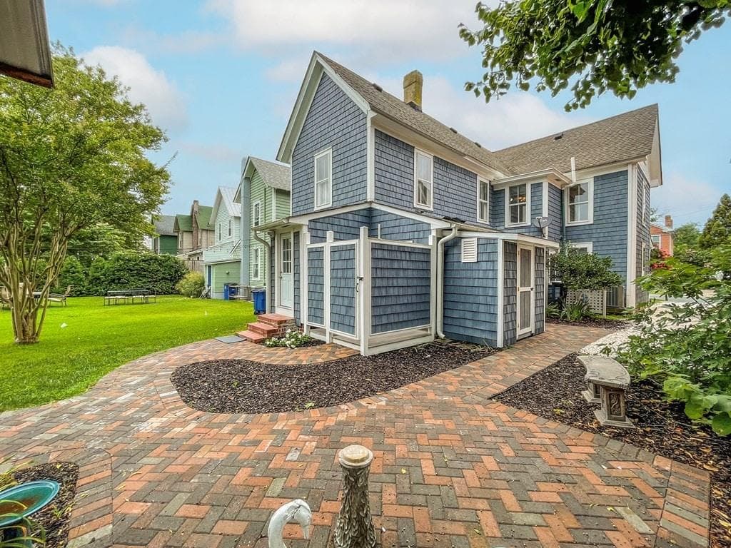 The backyard boasts a covered dining space, a blackstone grill, outdoor shower, and a shed full of beach toys